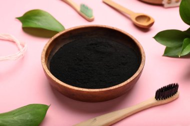 Aktif kömür diş tozu ve pembe arka planda diş fırçası olan bir kase.