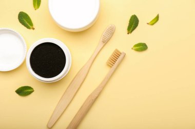 Aktif hale getirilmiş kömür diş tozu ve sarı arkaplanda diş fırçası olan kavanoz.