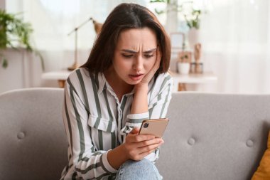 Odadaki koltukta cep telefonu mesajı okuyan üzgün bir kadın.