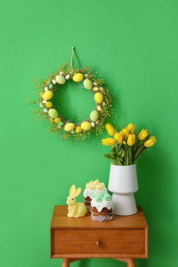 Paskalya pastası, tavşan ve vazo. Masanın yanında renkli duvarlı laleler ve çelenk.