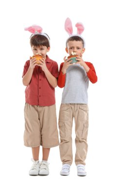 Tavşan kulaklı şirin çocuklar ve beyaz arka planda Paskalya pastaları.