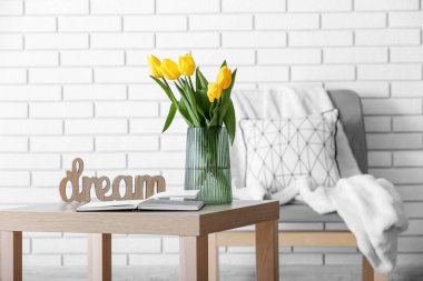Laleli vazo, açık kitap ve beyaz tuğla duvarın yanındaki masada DREAM.