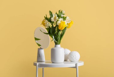 Çiçekli vazo, ayna ve renkli duvarın yanındaki masada şık bir dekor.