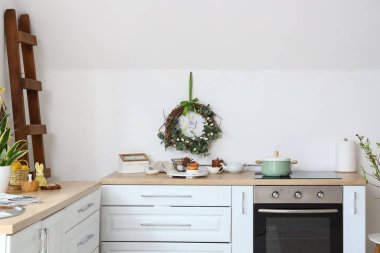 Mutfak tezgahında farklı aletler ve beyaz duvarın yanında Paskalya dekorasyonu.