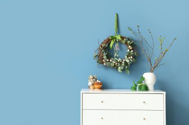 Ağaç dalları, pasta ve Paskalya dekoru olan vazolar renk duvarının yanındaki çekmecelerde.