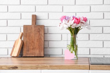 Çiçekli vazo ve beyaz tuğla duvarın yanındaki mutfak tezgahında boş kart.