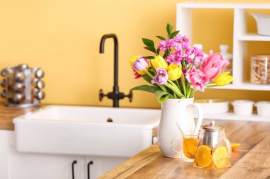 Çiçekli sürahi, mutfak tezgahında çaydanlık ve bardak.