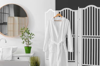 Beyaz bornozlu, aydınlık banyonun modern iç mekanı.