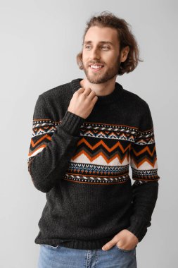 Gri arka planda örülü süveter giyen yakışıklı genç adam.