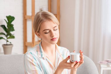 Kanepede oturan ve kablosuz taşınabilir hoparlöre bakan genç bir kadın.