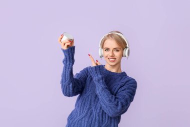 Kulaklıklı kadın menekşe arkaplanda kablosuz portatif hoparlöre bakıyor.