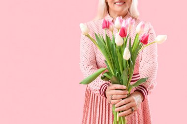 Gülümseyen olgun bir kadın pembe arka planda bir buket lale tutuyor, yakın plan. Uluslararası Kadınlar Günü kutlamaları