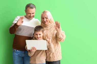 Büyük annesi ve büyük babasıyla yeşil arka planda video sohbeti yapan küçük bir çocuk.