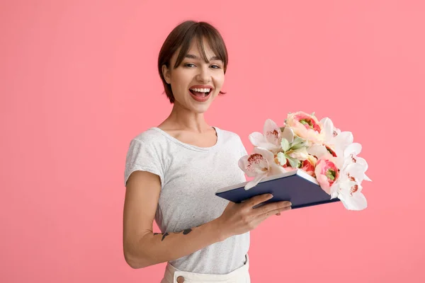 Schöne Junge Frau Mit Buch Und Blumen Auf Rosa Hintergrund — Stockfoto