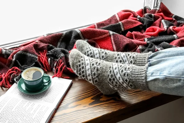 穿着保暖袜子的女性腿 一杯咖啡 打开一本关于窗台的书 供暖季节的概念 — 图库照片