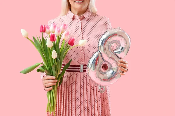 Olgun bir kadın pembe arka planda bir buket lale ve balon tutuyor. Uluslararası Kadınlar Günü kutlamaları