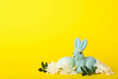 Güzel Paskalya tavşanı, sarı arka planda boyanmış yumurta ve çiçekler.