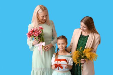 Genç kadın, küçük kızı ve annesi mavi arka planda hediyeler.