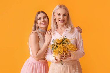 Annesi ve sarı arka planda mimoza çiçekleri olan genç bir kadın.