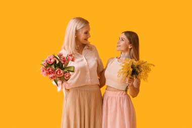 Annesi ve sarı arka planda çiçekleri olan genç bir kadın.