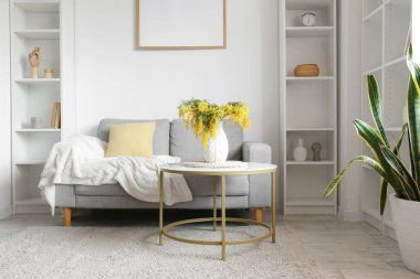 Mimoza çiçekli vazo ve oturma odasının içindeki masada bir kanepe.