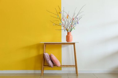 Masada paskalya yumurtaları ve odanın renk duvarının yanında yastıklar olan ağaç dalları.