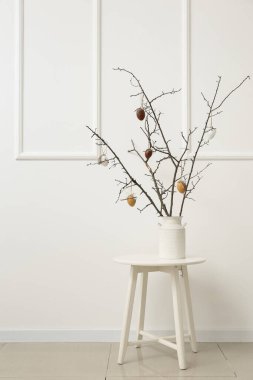 Ağaç dalları ve Paskalya yumurtaları olan vazo, odanın ışık duvarının yanındaki masada.