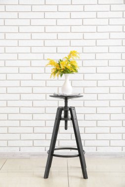 Mimoza dalları olan bir vazo. Odadaki hafif tuğla duvarın yanındaki masada.