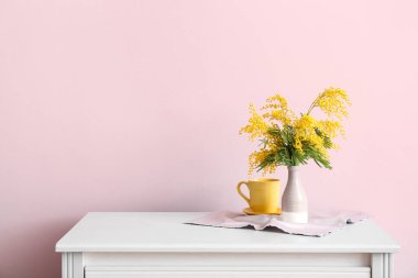 Güzel mimoza dalları olan vazolar ve odadaki renk duvarının yanındaki çekmecelerin üzerindeki fincanlar.