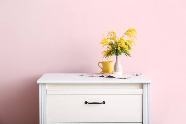 Güzel mimoza dalları olan vazolar ve odadaki renk duvarının yanındaki çekmecelerin üzerindeki fincanlar.