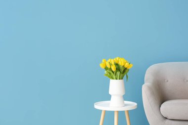 Renk duvarının yanındaki masada laleler olan rahat bir koltuk ve vazo.
