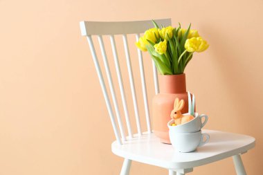 Laleli vazo ve renkli duvarın yanında Paskalya tavşanları olan fincanlar.