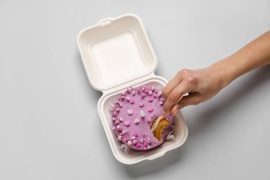 Gri arka planda plastik beslenme çantasında lezzetli bento pastası yiyen bir kadın.