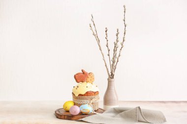 Wooden board with tasty Easter cake, eggs and pussy willow branches on light background