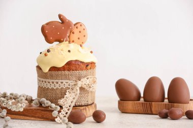 Kurabiyelerle süslenmiş lezzetli Paskalya pastası ve açık arkaplanda çikolatalı yumurta.