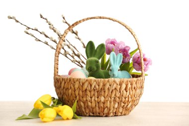 Basket with Easter bunnies, eggs, pussy willow branches and tulip flowers on light background