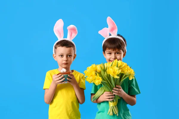 かわいいウサギの耳 イースターケーキと青い背景の花を持つ男の子 — ストック写真