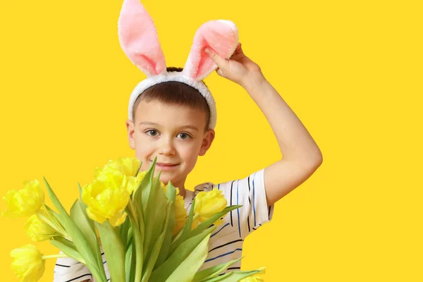 黄色の背景にウサギの耳と花を持つかわいい男の子 イースターのお祝い — ストック写真
