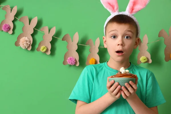 緑の背景にウサギの耳とイースターケーキと驚きの小さな男の子 — ストック写真