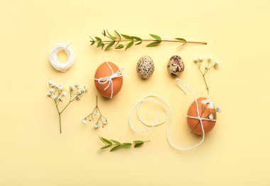 Sarı arka planda Paskalya yumurtası, ip ve çiçek kompozisyonu
