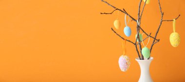 Vazodaki ağaç dallarına asılı Paskalya yumurtaları turuncu arkaplan ve metin için yer var.