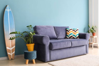 Mavi kanepesi, çiçekleri ve sörf tahtası olan şık bir oturma odası.