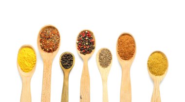 Beyaz arka planda farklı baharatlara sahip tahta kaşıklar, yakın plan.