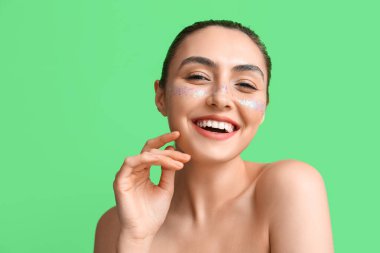 Yeşil arka planda yaratıcı makyajlı gülümseyen genç bir kadın.