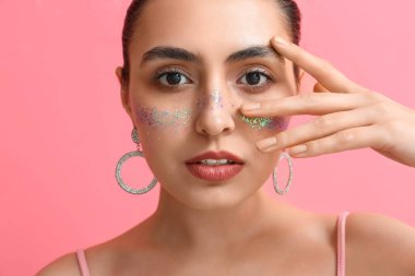 Yaratıcı makyajlı ve elleri pembe arka planda olan genç bir kadın.