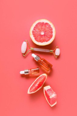 Gerekli yağ şişeleri, yüz masajı aracı ve arkaplanda greyfurt parçaları bulunan kompozisyon