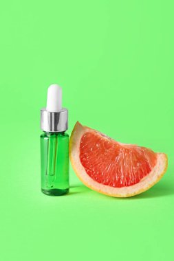 Yeşil arka planda bir şişe gerekli yağ ve greyfurt dilimi.