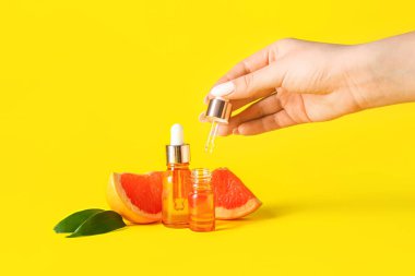 Sarı arka planda greyfurt yağı şişeleri olan kadın el, yakın plan.