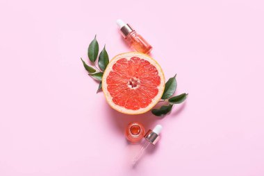 Pembe arka planda gerekli yağ şişeleri, bitki yaprakları ve greyfurt bileşimi