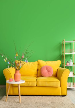 Masada, kanepede ve oda duvarının yanındaki rafta paskalya yumurtaları olan ağaç dalları.